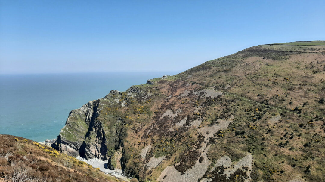 A massive and smooth heather-covered hill sweeps down to the sea. A path slopes down across the face of the hill.