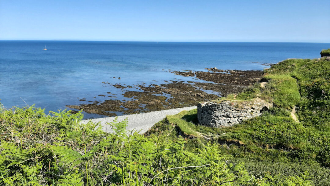 Blue sky, blue sea, low rocks, green grass and bushes.