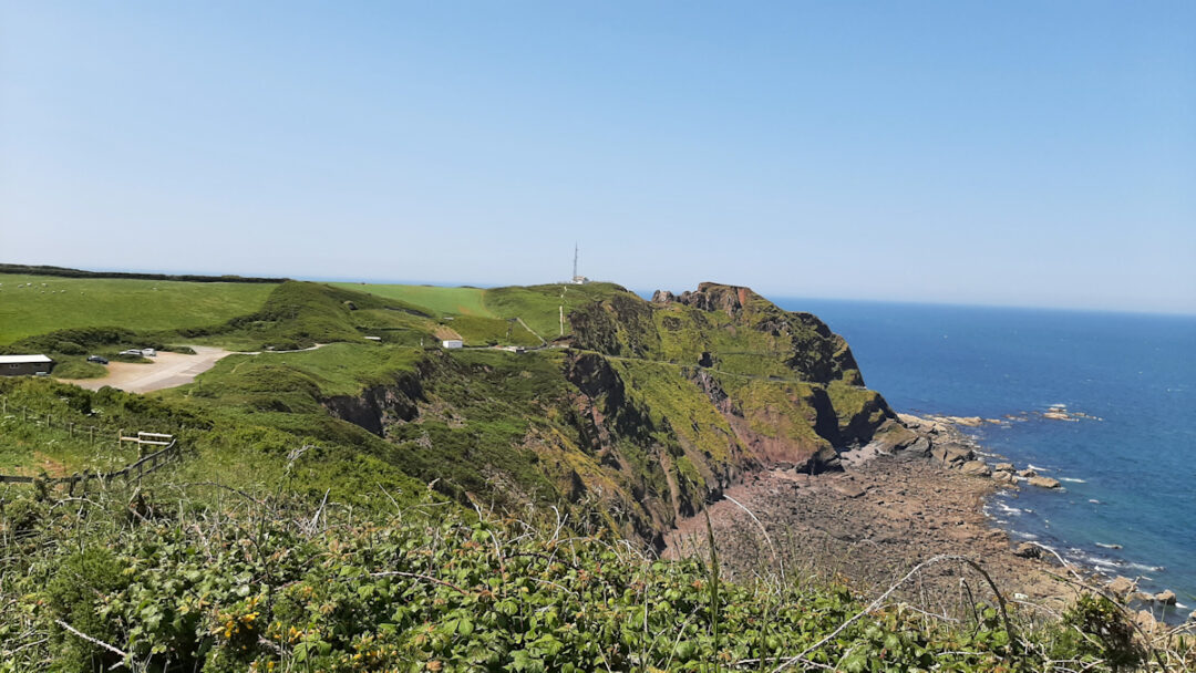 Coast with cliffs, with a car park and aerial masts in the distance