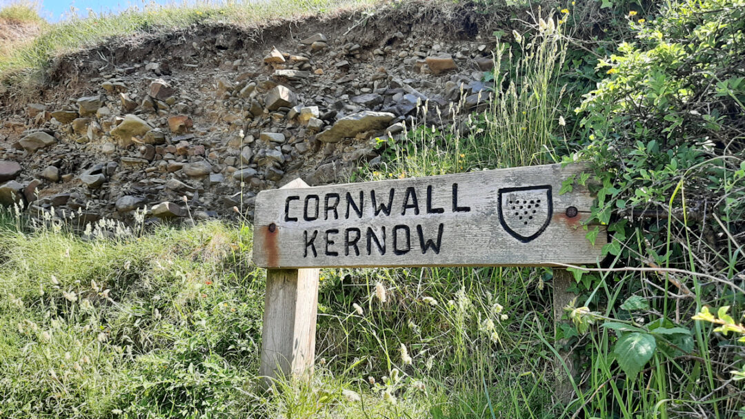 A wooden sign with the words "Cornwall Kernow" in clear capital letters with a shiueld showing the coat of arms of the county