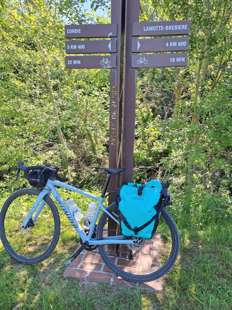 A blue bike with blue rear panniers leaning against a signpost