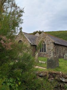 A small traditional stone church partially screened on the left by tees and bushes