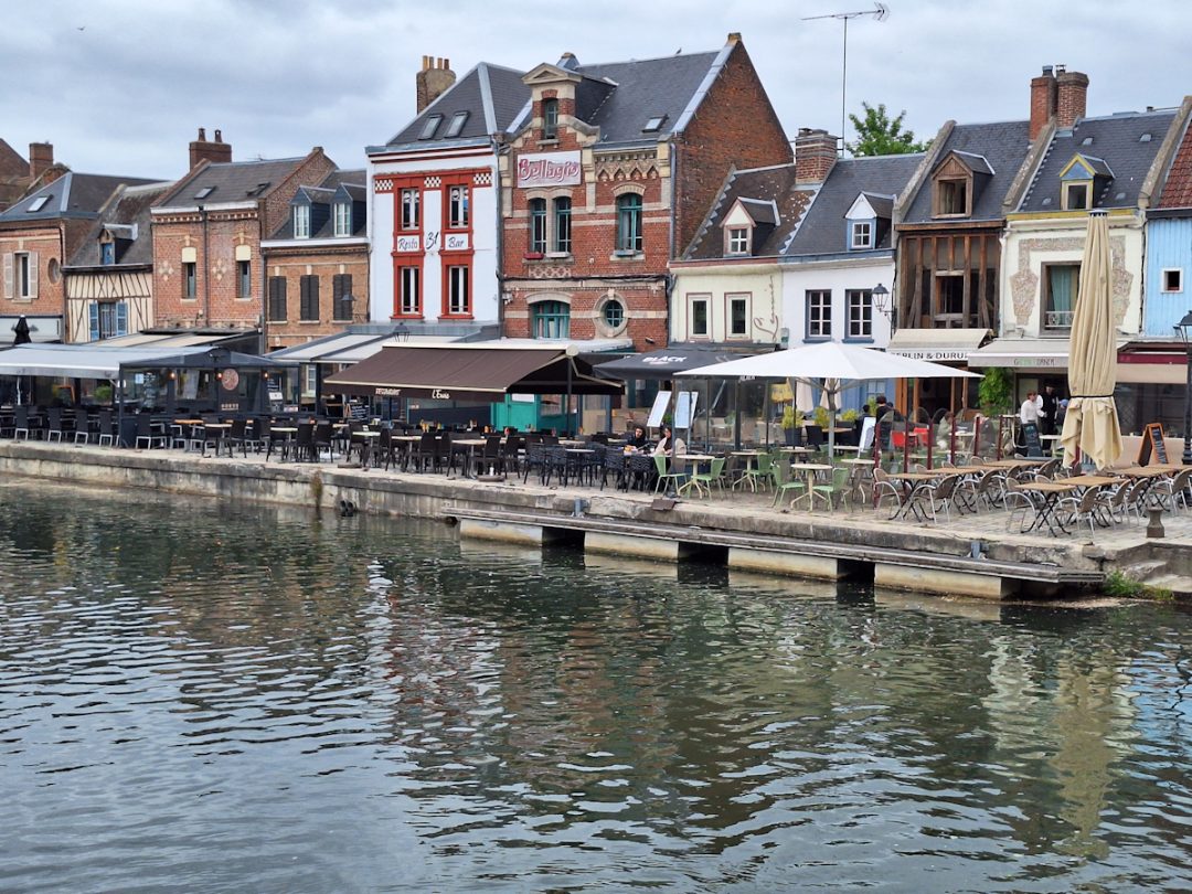 A row of cafés on the side of a canal with a variety of buildings behind