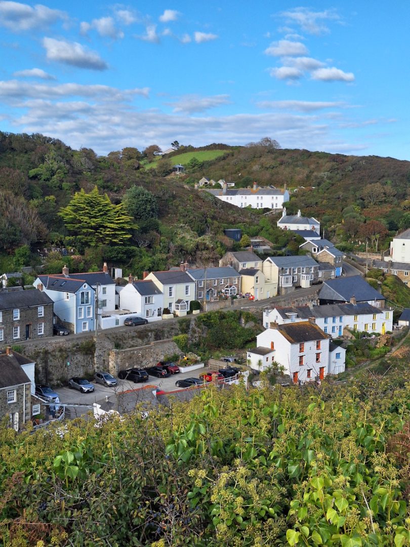 White cottages with grey roofs nestle in a narrow green valley under a blue sky with a few scattered clouds.