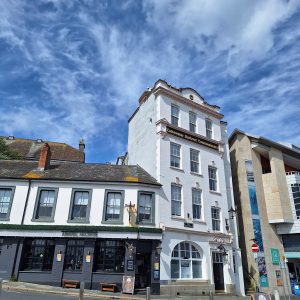 A pub, a tall white 4-storey building and part of a modern brick building seen from a low angle under a blue sky speckled with white clouds.