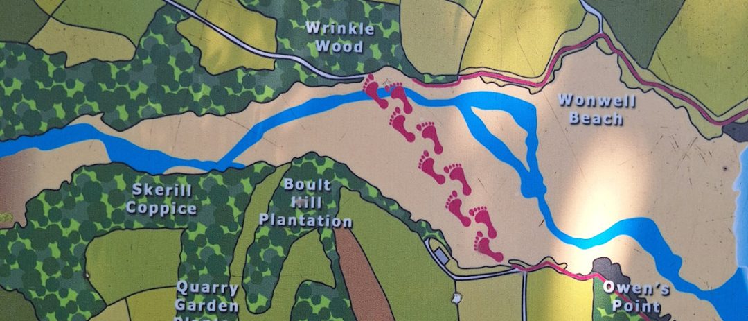 Part of an explanatory board showing the line to take when wading the Erme estuary at low tide. It is shown as stylised footprints across yellow sand and a blue stream.